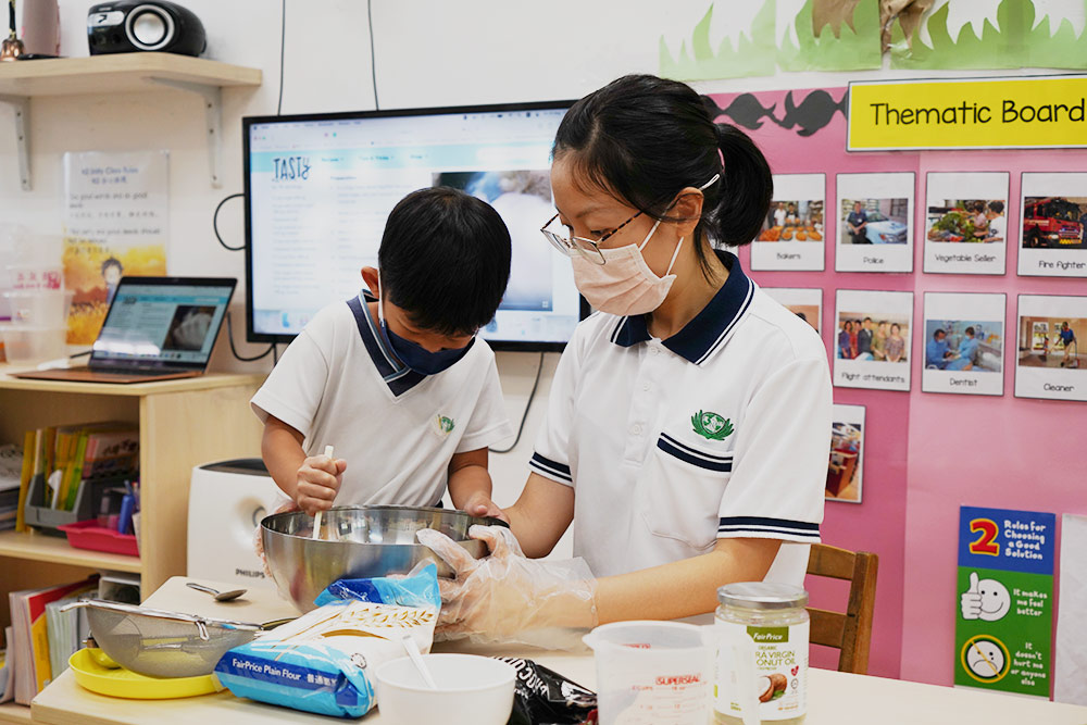 A kid attempts boldly with the help of his teacher. Everyone works together and experiences the fun of baking.  (Photo by Chan May Ching)